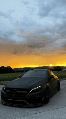 a black mercedes is parked on the side of the road at sunset