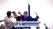 a hockey player is surrounded by fans and a sign says let 's go !!!