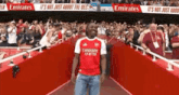 a man in a red emirates fly better jersey is walking down a red aisle in front of a crowd .