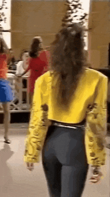 a woman in a yellow jacket and black pants is standing in front of a group of women .