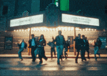 a group of people dancing in front of a building with a sign that says " just call my name out loud "