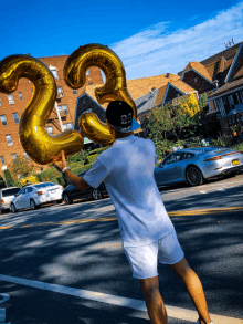 a man in a white shirt and shorts is holding balloons in the shape of the number 23