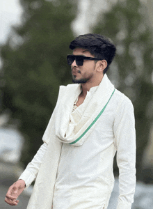 a man wearing sunglasses and a white shirt with a green sash around his neck