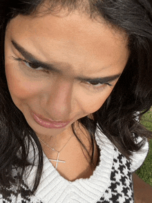 a woman wearing a cross necklace looks down at something