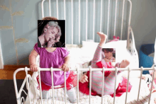 two little girls are playing in a crib with a picture of a man on the wall behind them