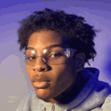 a young man wearing safety glasses and a grey hoodie looks at the camera