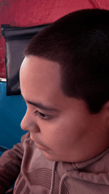 a close up of a young boy 's face with a red wall in the background