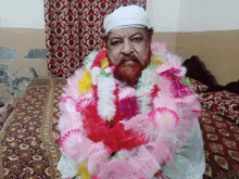 a man with a beard is wearing a white turban and a pink and yellow flower garland around his neck