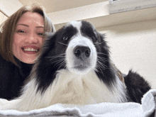 a black and white dog laying on a white towel next to a smiling woman