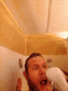 a man with a beard is taking a shower with a shower head