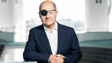 a bald man wearing a blue suit and white shirt has an eye patch on his eye