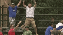a group of men are standing on a fence with their arms in the air