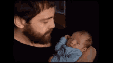 a man with a beard is holding a newborn baby in his arms .