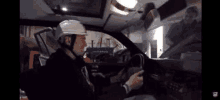 a man wearing a hard hat is driving a car and using a tablet .