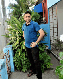 a man in a blue shirt stands in front of a garden