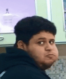 a man in a black hoodie is making a funny face while sitting in a kitchen .