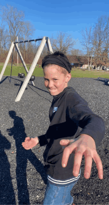 a young boy wearing a headband and a nike sweatshirt stands in front of a swing set