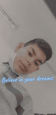 a young boy wearing a mask is taking a selfie with the words `` believe in your dreams '' .