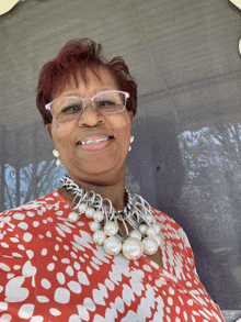 a woman wearing glasses and a pearl necklace smiles at the camera