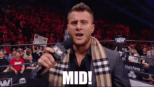 a man with a scarf around his neck holds a microphone and says " mid "