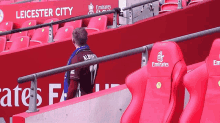 a man wearing a jersey that says alberts sits in a stadium with emirates seats