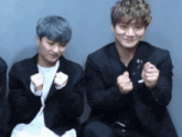 two young men are sitting next to each other and making a heart shape with their hands