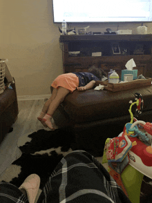 a little girl is laying on a ottoman in front of a television