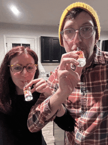 a man in a plaid shirt and a woman in glasses are drinking from small bottles