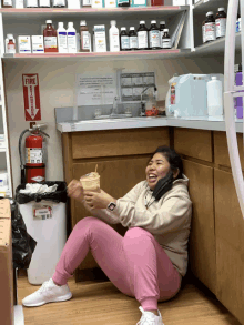 a woman is sitting on the floor in a pharmacy with a fire extinguisher in the background