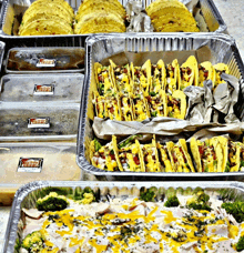 a tray of tacos sits next to a tray of broccoli and a tray of chicken