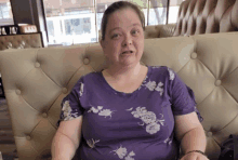 a woman in a purple floral shirt sits on a couch