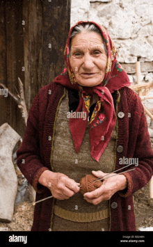 an elderly woman wearing a red head scarf is knitting and smiling for the camera