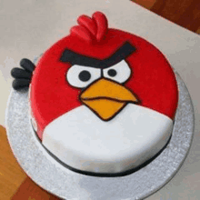 a red and white angry bird cake is sitting on a silver plate on a table .