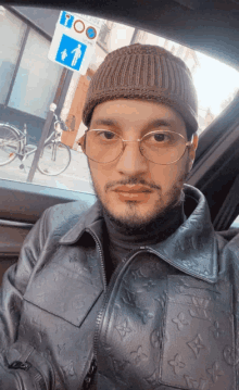 a man wearing glasses and a beanie is sitting in a car with a sign that says too