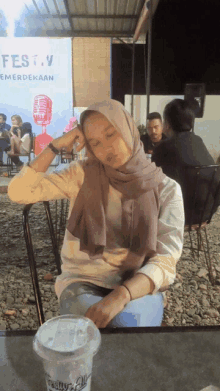 a woman in a hijab sits at a table in front of a sign that says fest.v emerdekaan