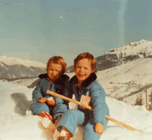 two children are sitting in the snow and one has a sticker on his jacket that says ' a ' on it