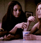 two women sit at a table with a cup of yogurt