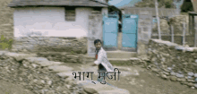 a man is standing in front of a stone wall with a blue gate and a sign that says ' bhaga mujji '