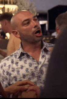 a bald man in a blue and white shirt is talking to a group of people .