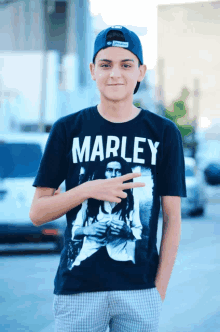 a young man wearing a black marley t-shirt stands with his hands in his pockets