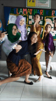 a group of women posing for a picture in front of a sign that says " selamat hari k "