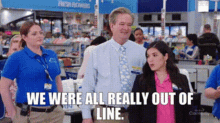 a man and two women are standing in a line at a grocery store . the man is wearing a tie .