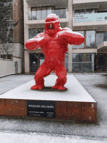 a statue of a red gorilla by richard orlinski in the snow