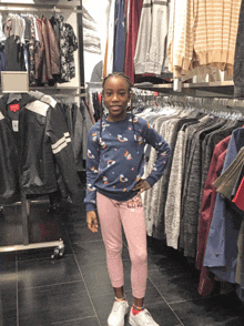 a little girl wearing a blue sweater and pink pants stands in a clothing store