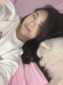 a woman laying on a bed with a white dog wearing a white shirt that says the