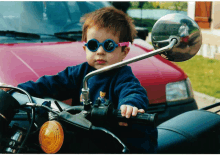 a young boy wearing sunglasses is riding a motorcycle