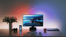 a desk with a computer monitor headphones a phone and a vase of flowers