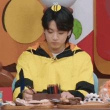 a young man is sitting at a table with a bee on his head and writing in a notebook .