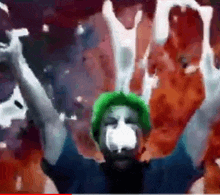 a man with a green hat and a white face is holding up his arms .