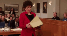 a woman in a red jacket is holding a piece of paper in front of a jury in a courtroom .